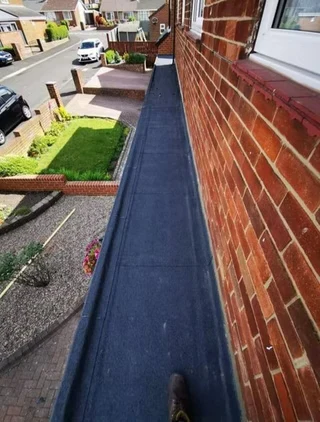 A high-angle view of a flat roof walkway beside a brick wall
